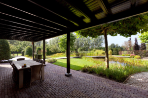 veranda aan de woning gevestigd om te genieten van een overdekt terras in de landschapstuin voorzien van een vijver welke zorgt voor een speelse waterpartij voorzien van borders met vaste struiken en planten omringt door strak vormgegeven gazon in Oudewater en Benschop