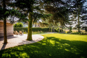 terras en zithoek voorzien van een natuur vijver voor een strakke tuin met een sfeervol karakter voorzien van vaste struiken en bomen omringt door een schitterend gazon